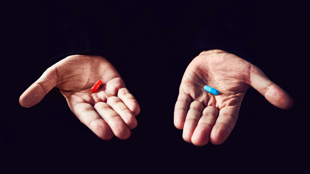 The image shows two hands with one red pill and one blue pills in the hands.