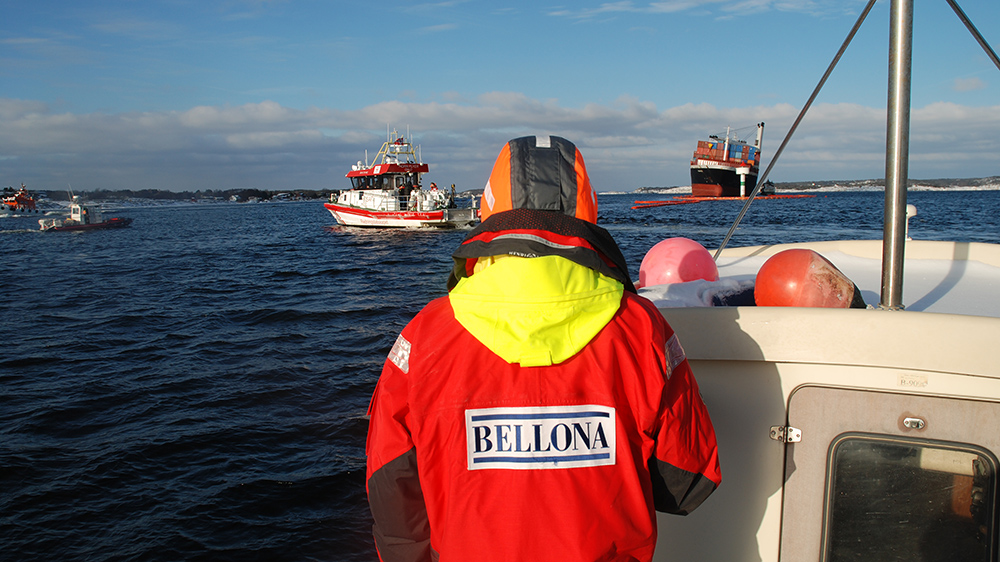 Image of Bellona activist on a boat at sea, wearing a high visibility vest with a Bellona logo, facing several other boats.