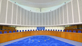 Bilde av en rettssal i Den europeiske menneskerettighetsdomstolen. EUs flagg som teppe.