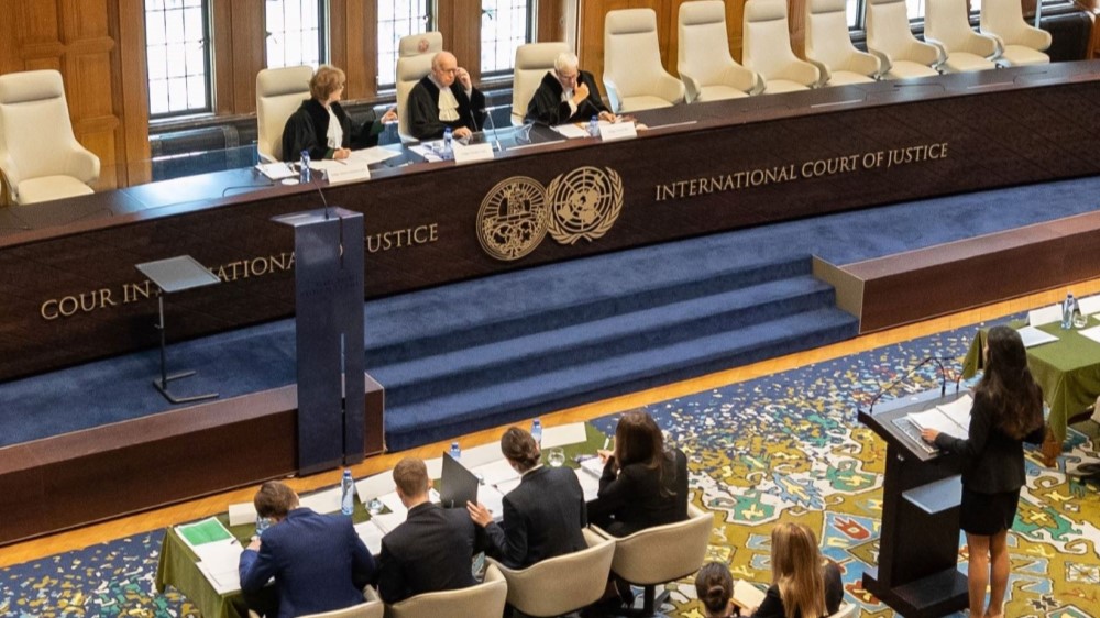 Three judges sit at a podium in the International Court of Justice, one student presents, and several others follow the moot