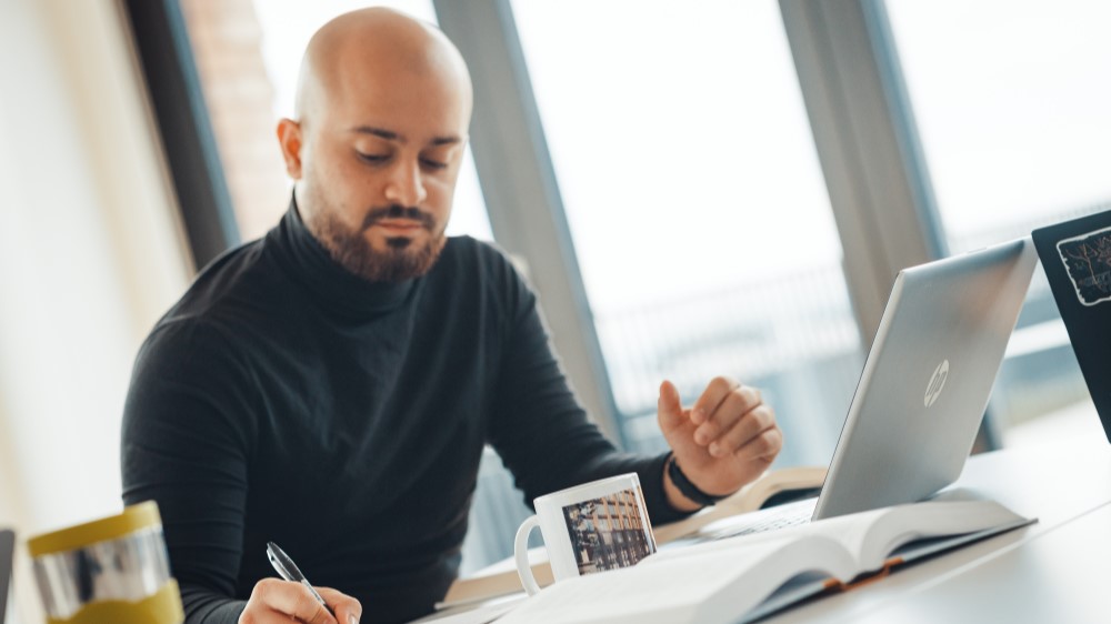 Student foran PC som noterer i notatbok