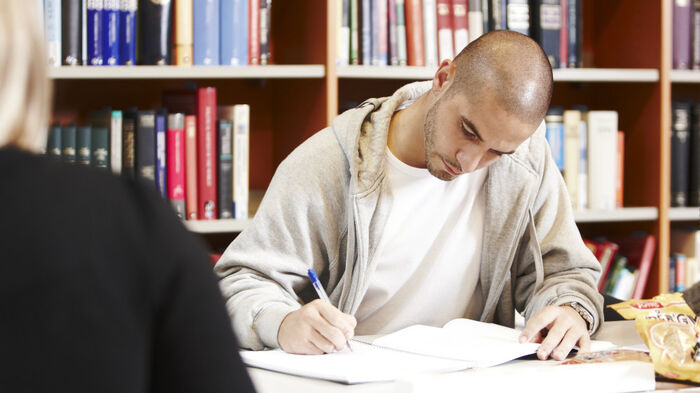 student som skriver, sittende i et bibliotek