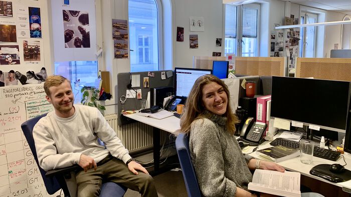 bilde av to personer, gutt og jente, jobber hos jussbuss, sitter i kontorstol på plassene sine