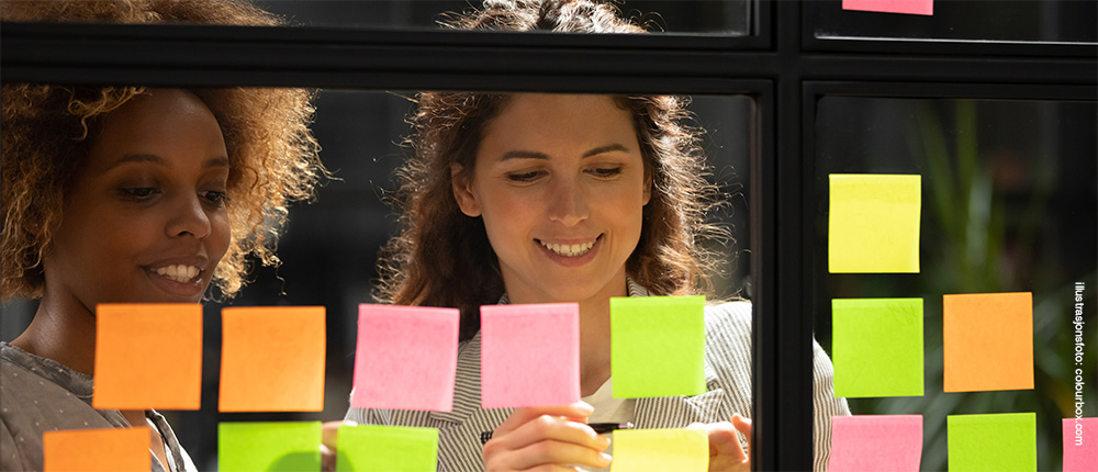 To personer fester post-it lapper på glassvegg.