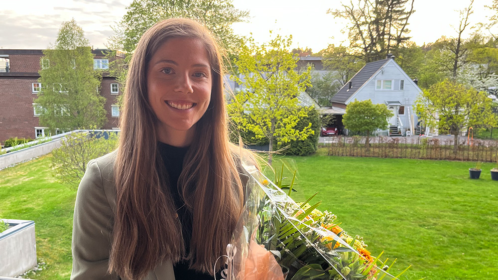 Kvinne holder en bukett med blomster og smiler til kamera i hage.