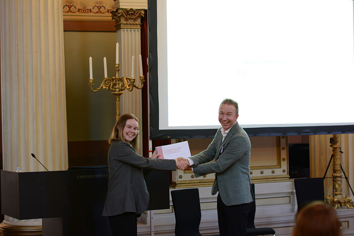 Dame overrekker en mann en rapport og tar hverandre i hånden.