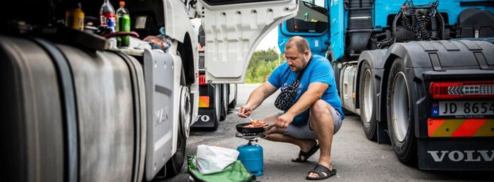 Mann kokkelerer mat mellom to trailere på veien.