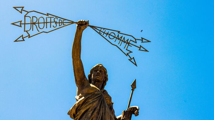 Photo taken against a blue sky of a bronze statue of a goddess holding arrows with the  words "droits de l'homme". 