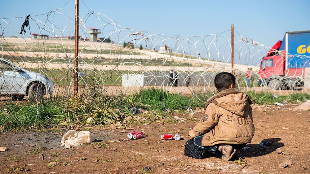 A boy kneels on the ground beside the border fence near seperating his country Syria and Turkey.