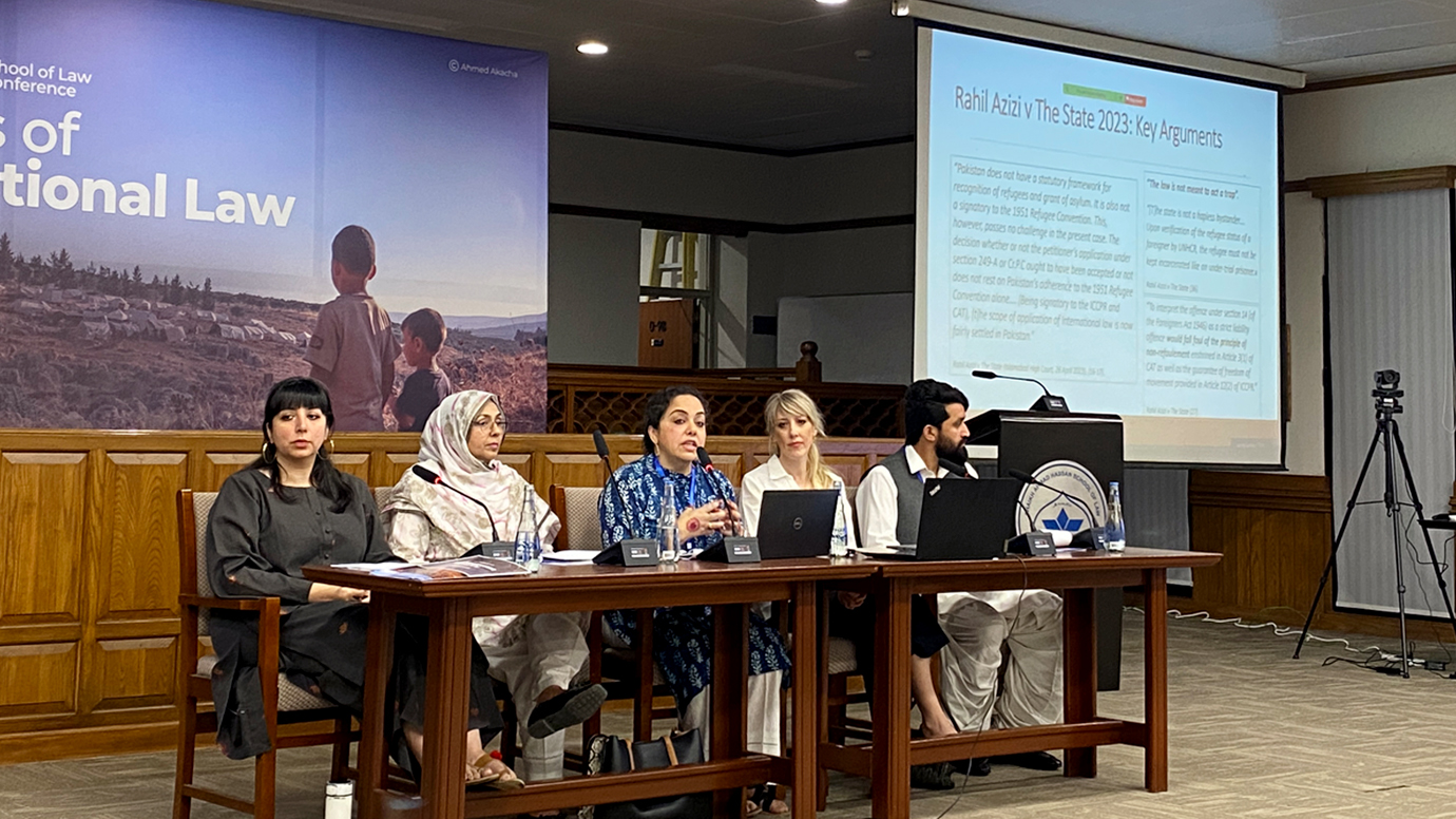 Dr. Arjumand Bano Kazmi are sitting with the other panalist on stage while she presents her research on Afghan refugees in Pakistan.