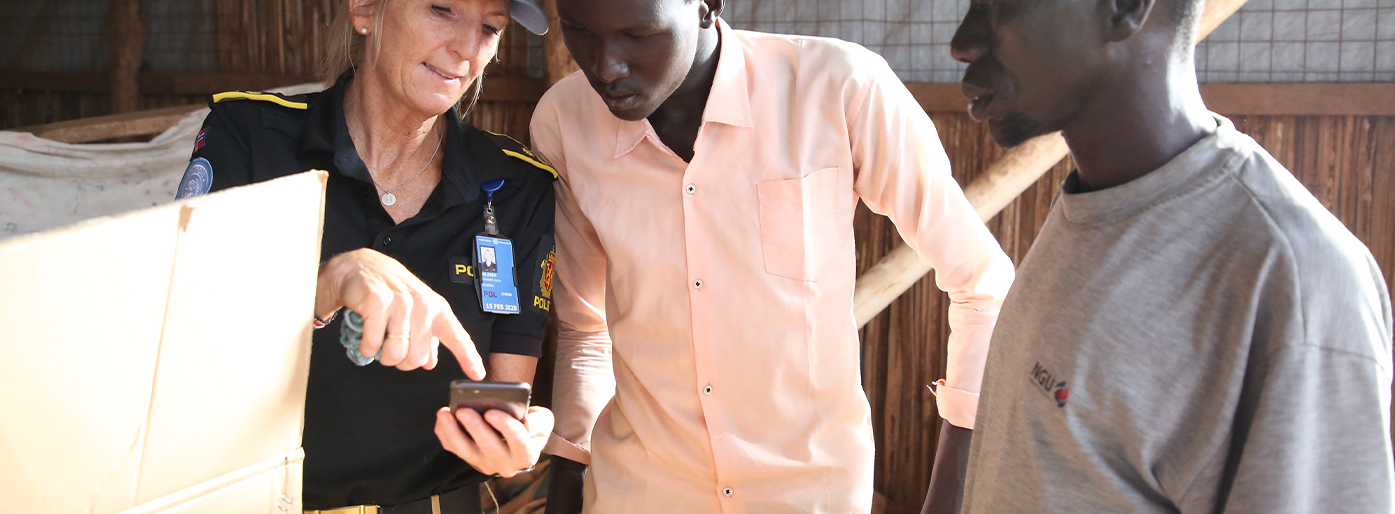 Norsk politikvinne viser frem noe på mobilen til to sudanske menn i et fotografi.