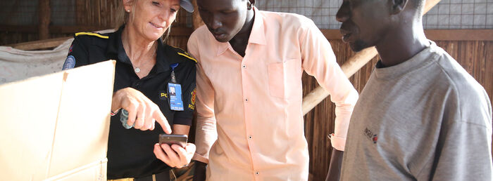 Norsk politikvinne viser frem noe på mobilen til to sudanske menn i et fotografi.