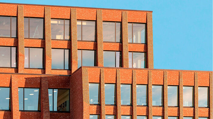 Foto av et hjørne av en bygning med rød murfasade mot en blå himmel