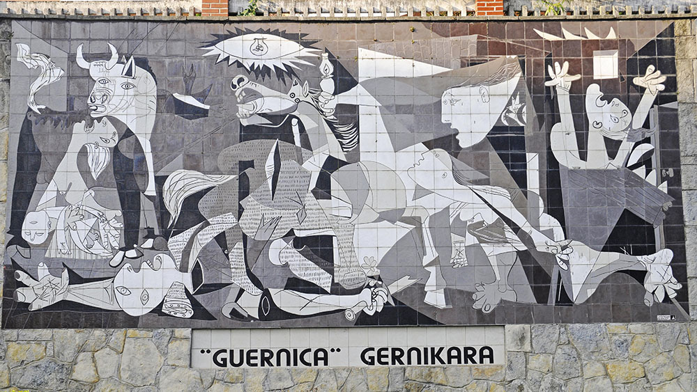 Mural in black, white and gray depicting people and cows. In front you can see a short hedge and a pavement.