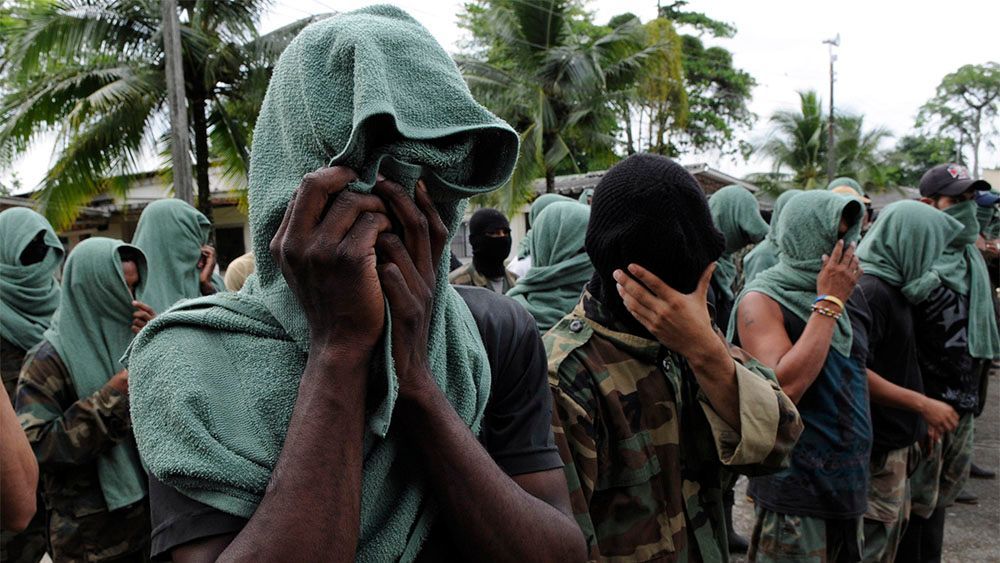 Several people lined up in line who cover their faces and have their heads covered with green textiles to hide their identity.
