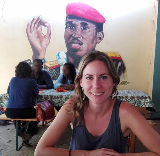 Bildet viser postdoktor Eva Stambøl sittende ved et bord foran et veggmaleri av Thomas Sankara.