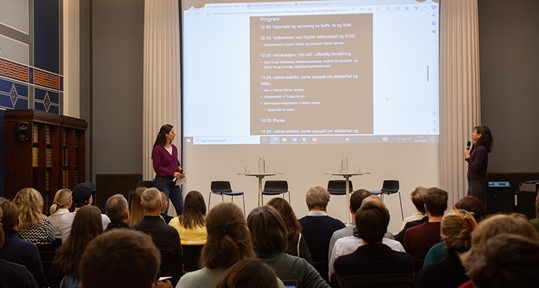 Bildet kan inneholde: ledd, stol, dress, offentlig tale, projeksjonsskjerm.