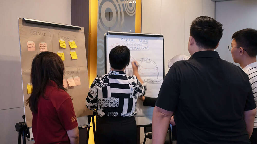 Four people standing in front of whiteboards, one of them writing