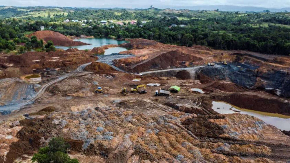 Arial photo of a nickel mine, featuring several vehicles, mounds of earth, and a small lake 