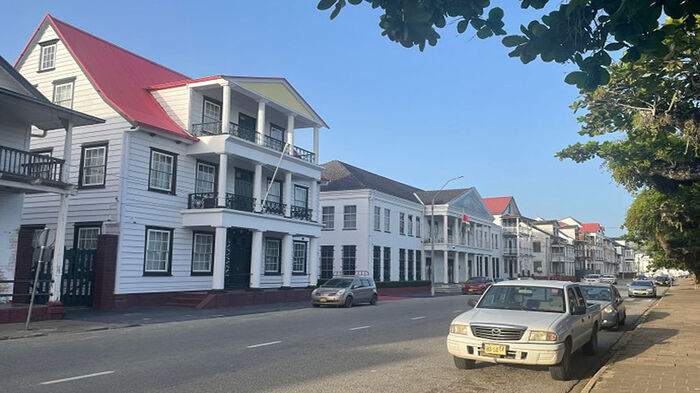 White wooden houses, trees, blue sky and a car parked in the street. 