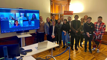 Group photo of conference participants, both physical attendants and online participants on a screen