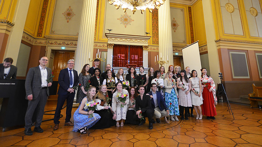 Group photo of the recent graduates and accompanying professors in the Gamle Festsal, a grandiose room at the University of Oslo