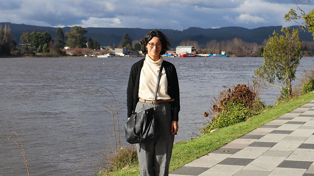 Photo of Dr. Torres in front of a large body of water, next to a brick path with trees on its edge