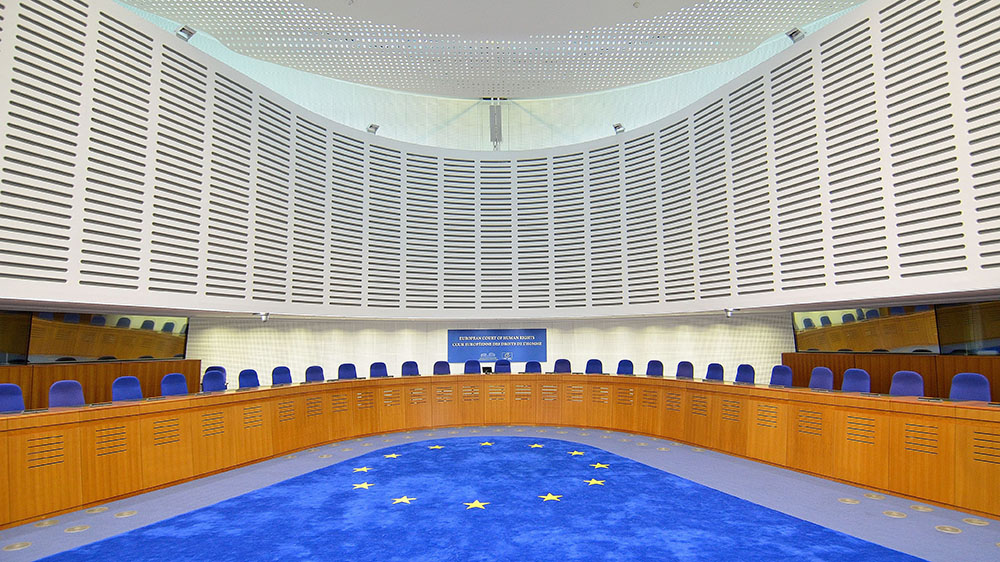 Bilde av en rettssal i Den europeiske menneskerettighetsdomstolen. EUs flagg som teppe.